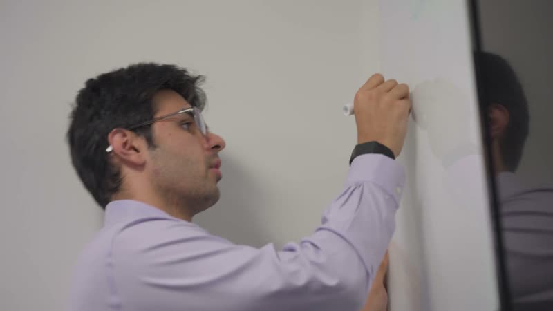 An analyst writing on a whiteboard in a bright office