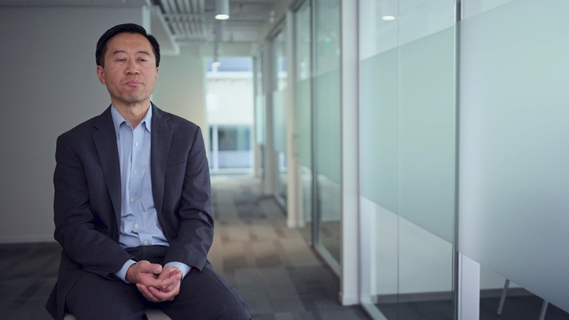 A man seated for an interview in an office corridor