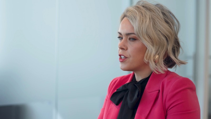 A woman in a pink blazer interviewed in a bright office